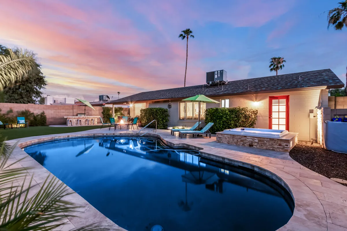 A vibrant backyard featuring a sparkling swimming pool, hot tub, lounge chairs, colorful umbrellas, and swaying palm trees. The atmosphere is lively and joyful, perfect for sunbathing, barbecuing, and gathering with friends or family, day or night.