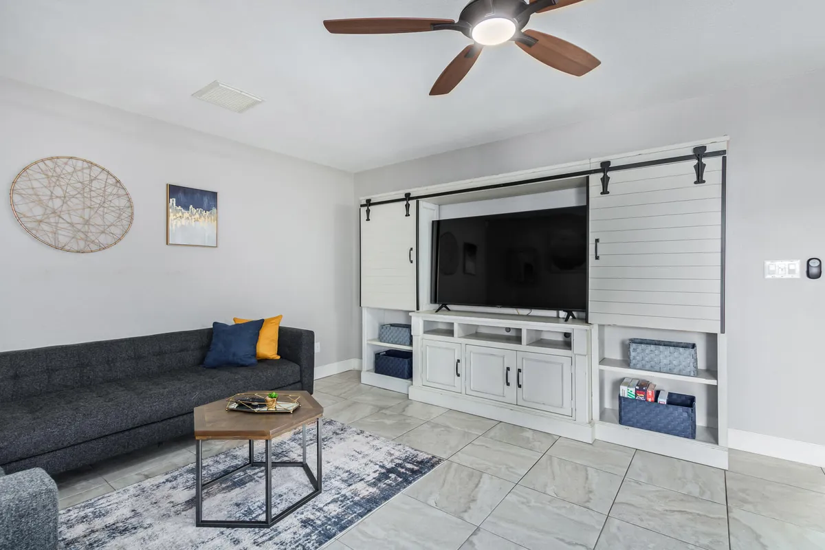 A spacious living room scene featuring a sofa, coffee table, television unit, and wall art. The setup is ideal for watching TV, socializing, and relaxing, with a comfortable open feel that fits a group setting.