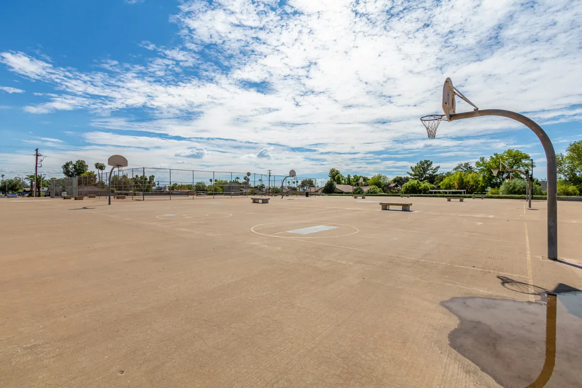 This exterior scene showcases basketball hoops and a well-maintained court surrounded by trees and fencing. The setting buzzes with the potential for pickup games and energetic community gatherings, echoing the sporting spirit highlighted in the section.