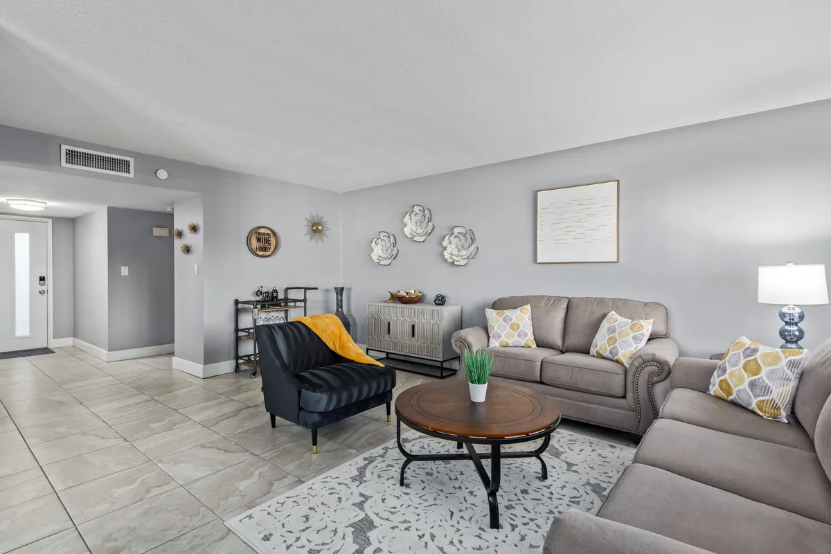 This image showcases a cozy living room with a circular coffee table, a sofa adorned with decorative pillows, an armchair draped with a throw blanket, stylish wall art, and a table lamp. The arrangement encourages social gatherings and relaxation, embodying a comfortable and inviting atmosphere.