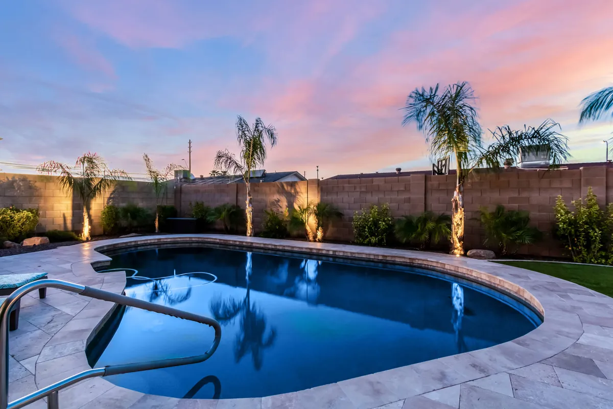 A tranquil scene showing a swimming pool surrounded by palm trees and landscaped areas, with the sky painted in sunset colors. The setting includes spaces for swimming, relaxing by the pool, and gathering in the evening, embodying a sense of serene celebration and enjoyment of Arizona's warm climate.