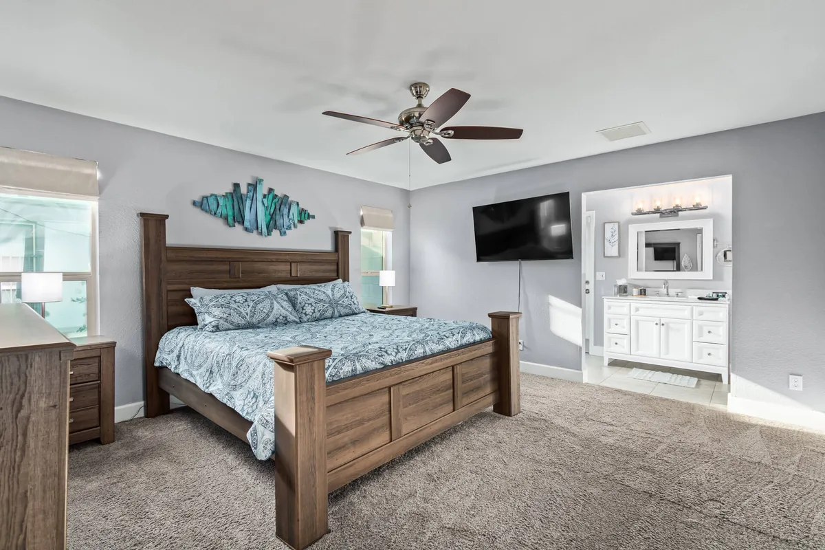 A spacious bedroom with a king-sized bed adorned in patterned bedding, complemented by wooden furniture and a wall-mounted television. Decorative wall art adds a touch of personality, and natural light streams softly into the room, creating a calm and inviting environment.