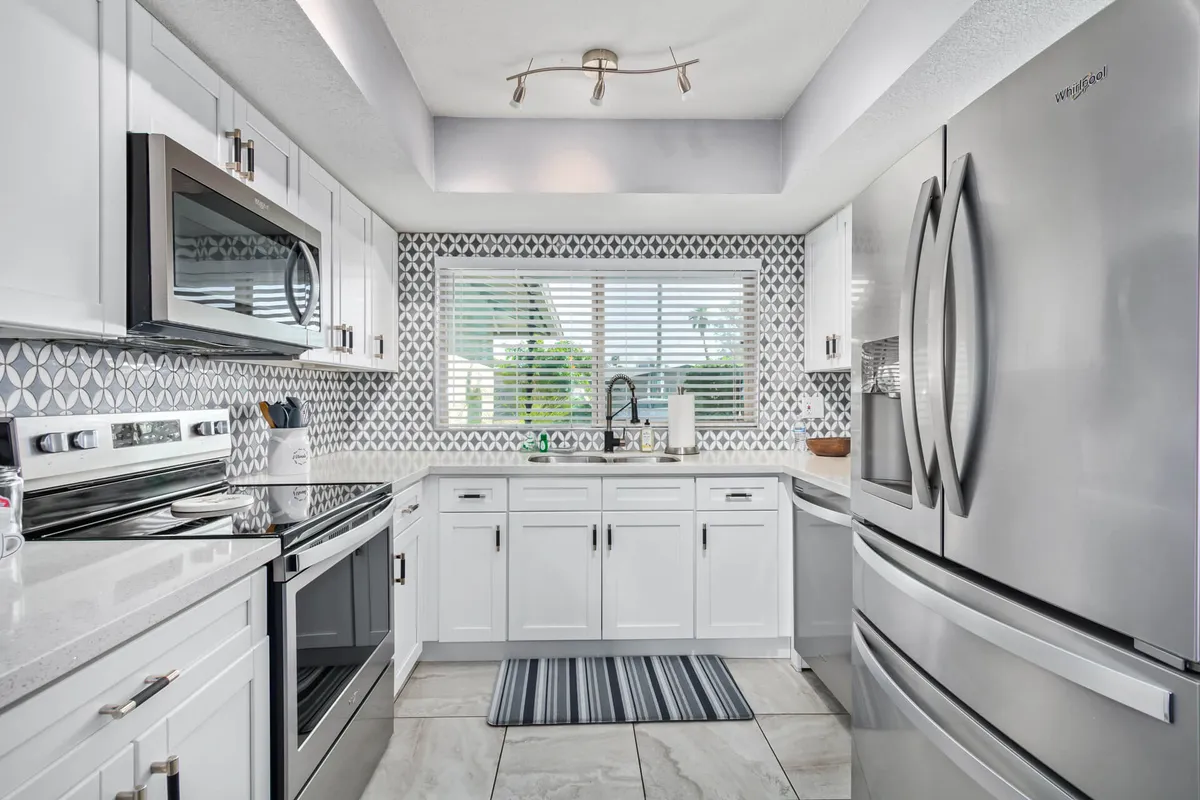 An inviting kitchen scene with modern appliances, a geometric backsplash, a prominent kitchen island, and a large window. The area is tailored for communal cooking and gathering, capturing a welcoming and stylish mood that encourages socializing and shared meals.