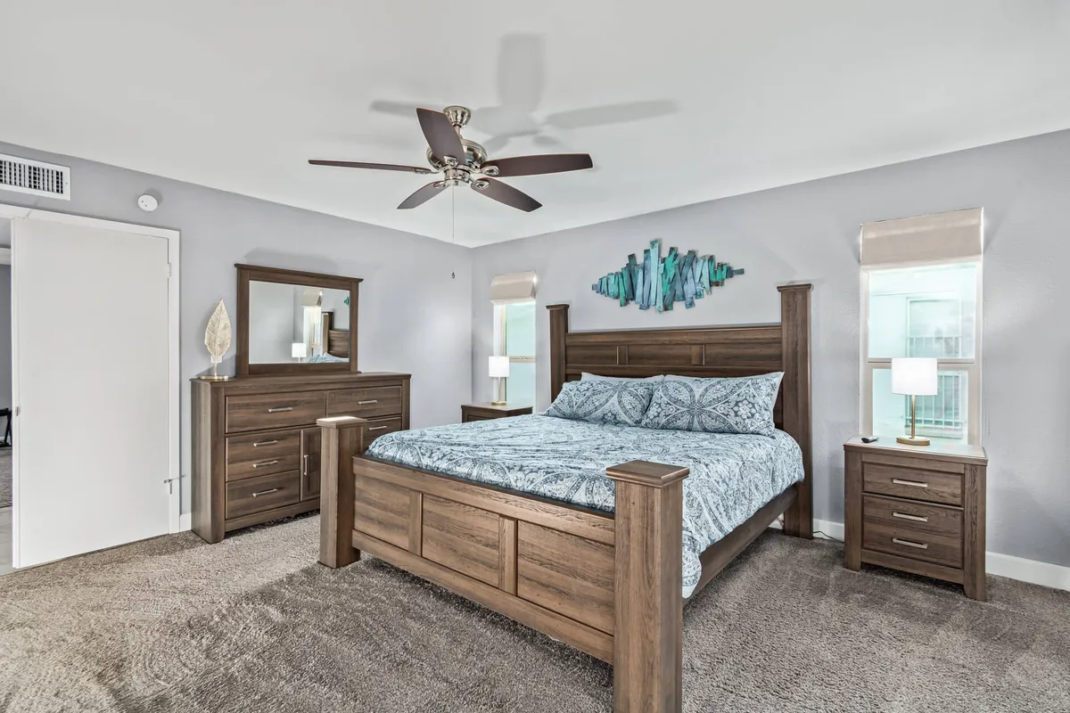 A serene bedroom featuring a king-sized bed with plush bedding and decorative wall art above the headboard. Nightstands with lamps on either side add a warm ambiance, while a dresser offers additional storage. The space is styled with subtle Southwestern touches, providing a peaceful atmosphere ideal for relaxation and rest.